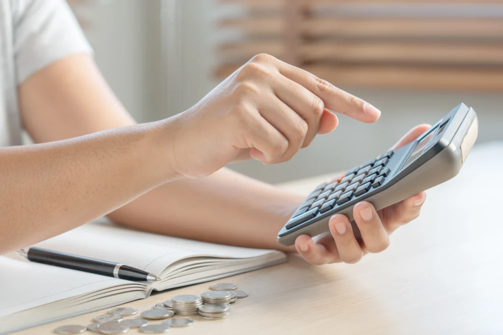 A Man setting his budget for hiring a nanny with the help of calculator and notebook.